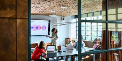 Mid adult woman delivering meeting in board room Female team leader standing in board room, providing feedback on business strategy to multi racial colleagues, forecasting and projecting